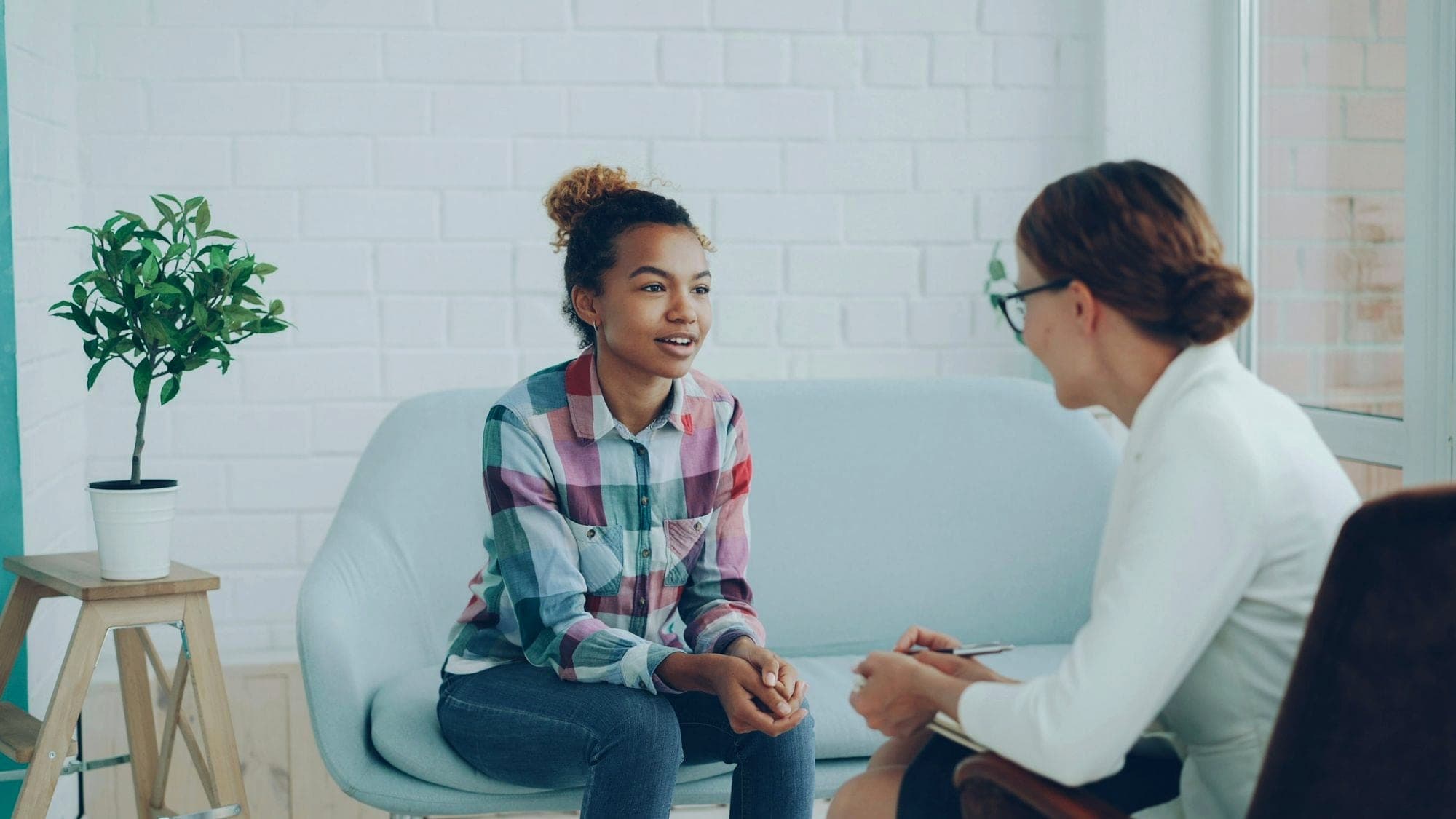 Two women talking on a sofa in a bright clinic