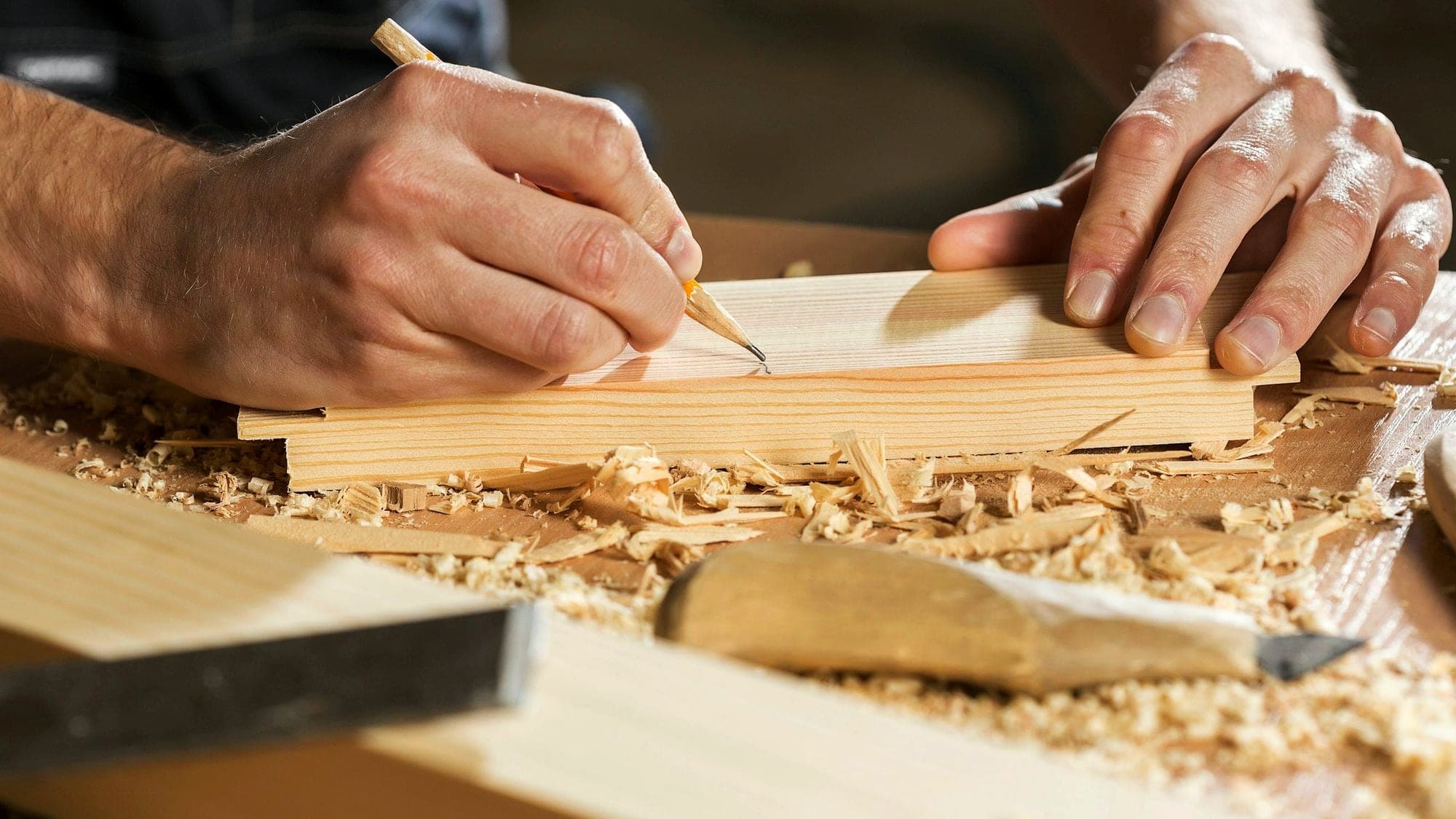 A woodworker marking a line on a board with a pencil