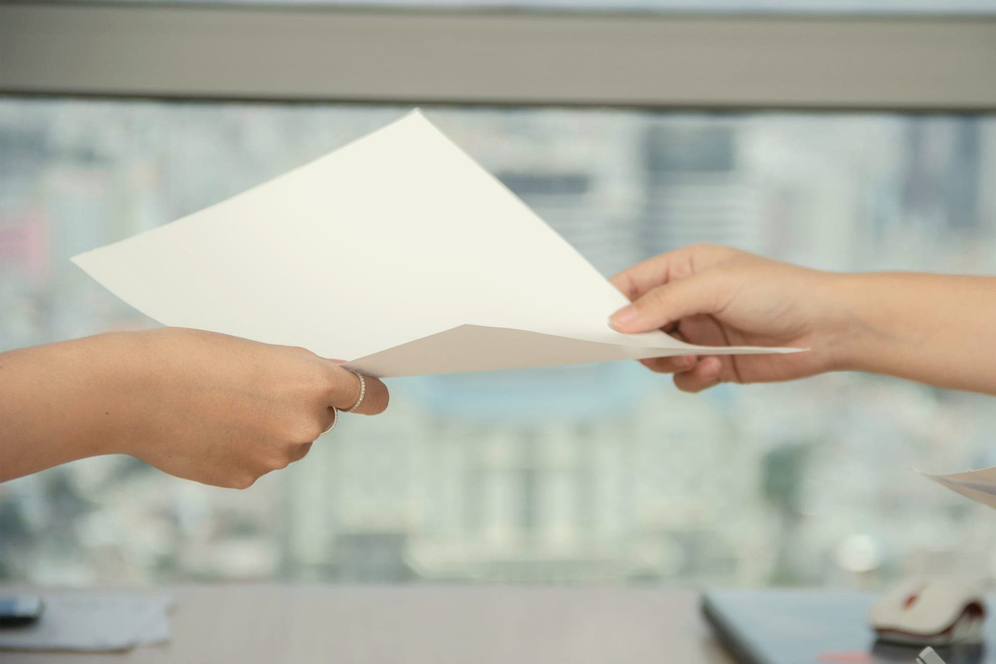 A sheet of paper passing from one hand to another in front of a window.
