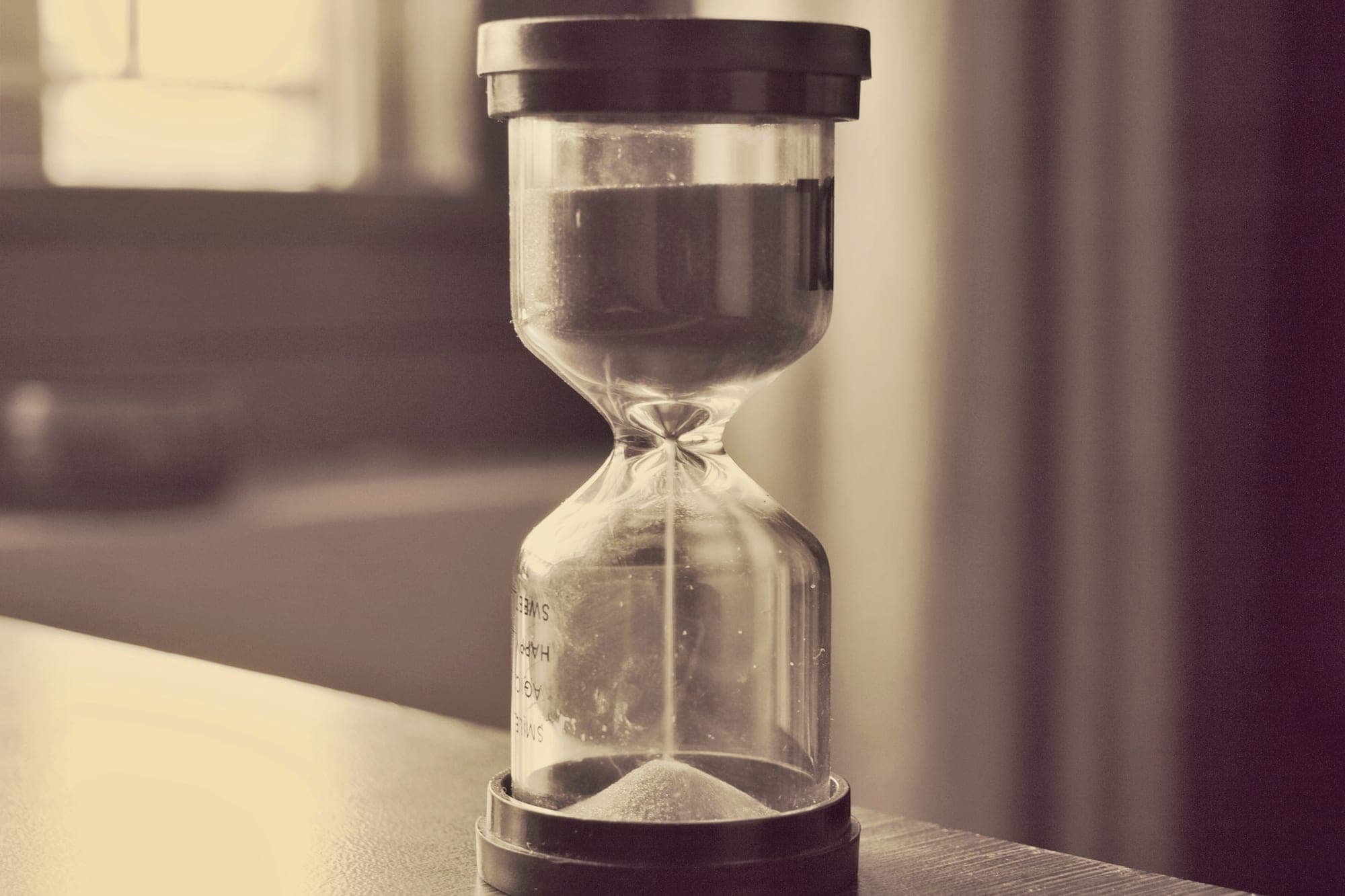 An hourglass on a table by a window, the sand running.