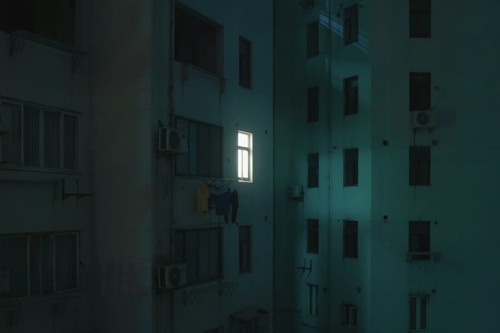 One lit window in a dark apartment block at night.
