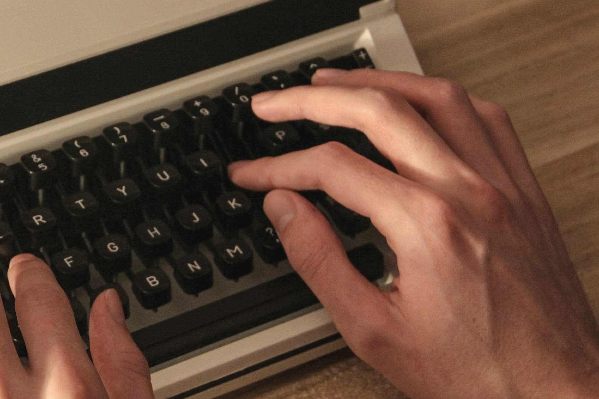 Two hands typing on a cream typewriter at a wooden desk.