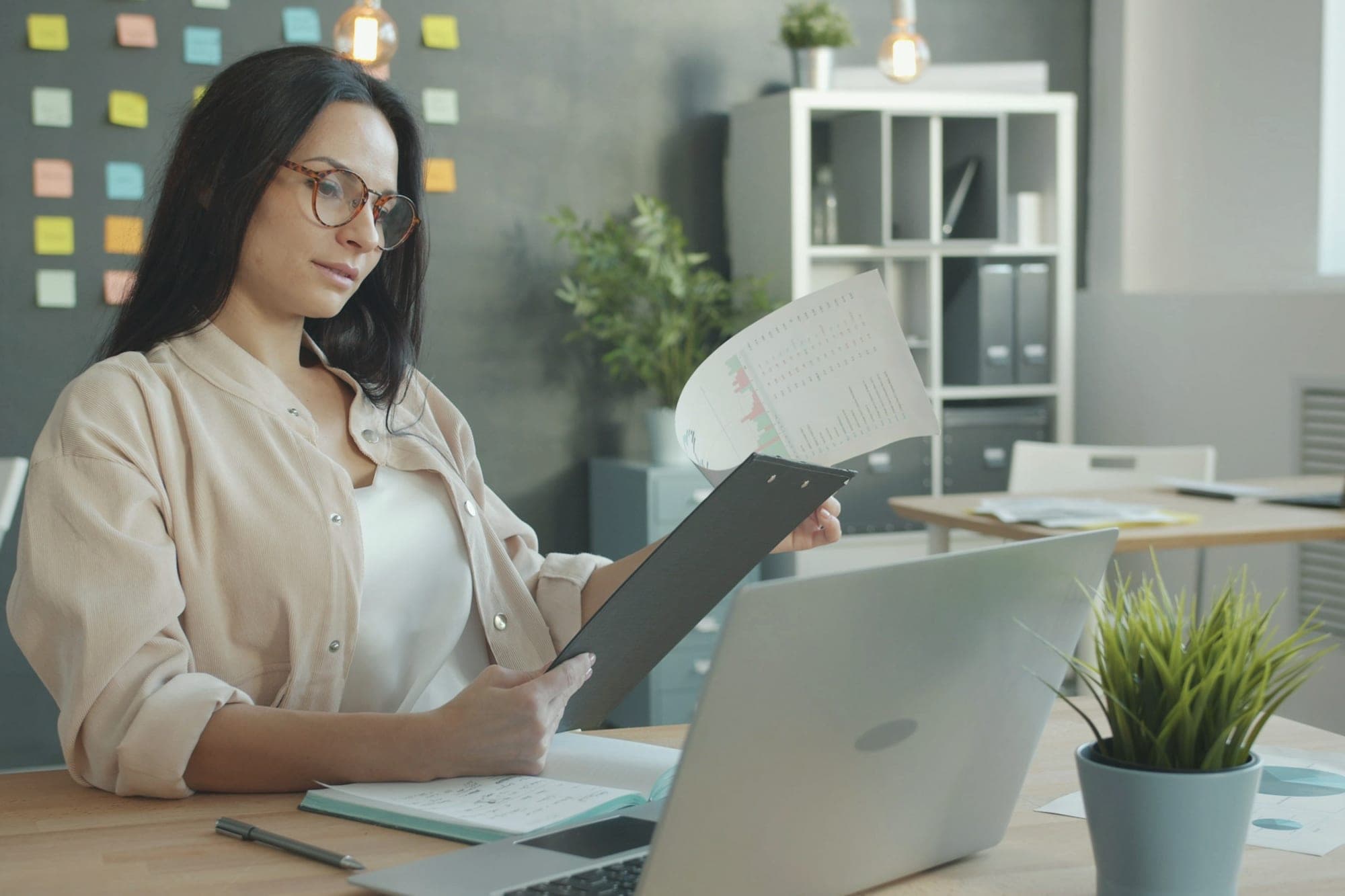 A woman at her desk reading a printed document on a clipboard
