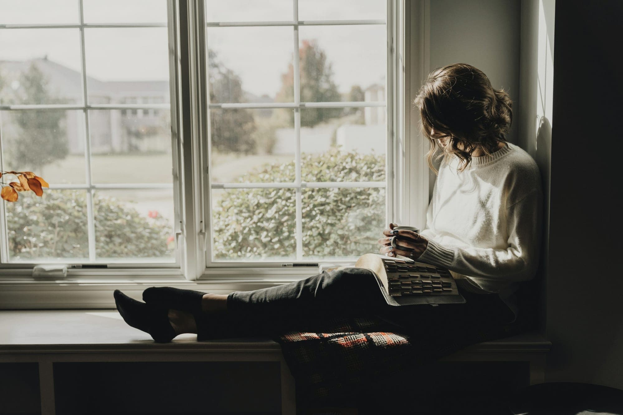 A woman reading on a window seat, light coming in from the garden