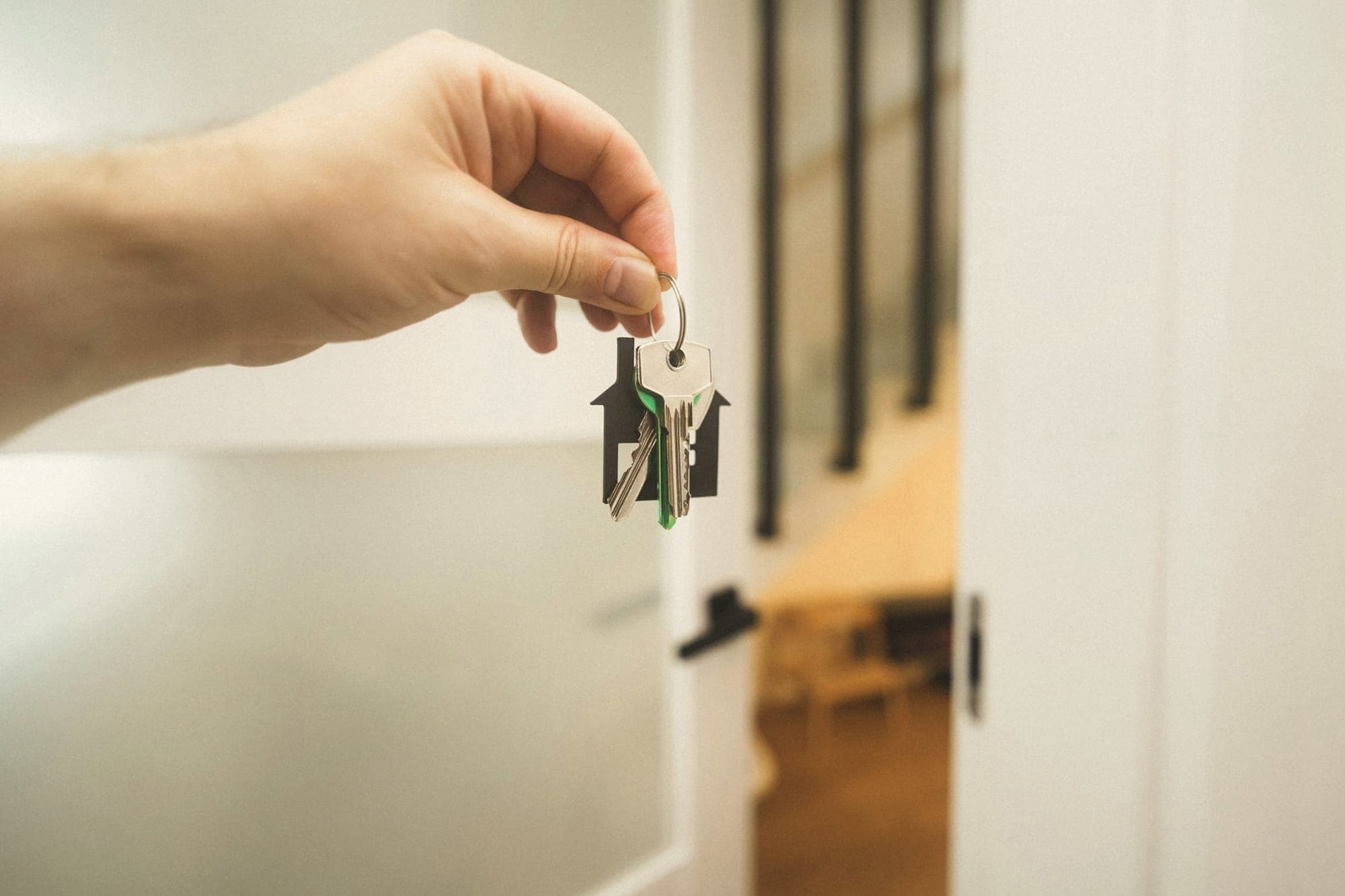 A hand holding up a set of house keys in a bright hallway