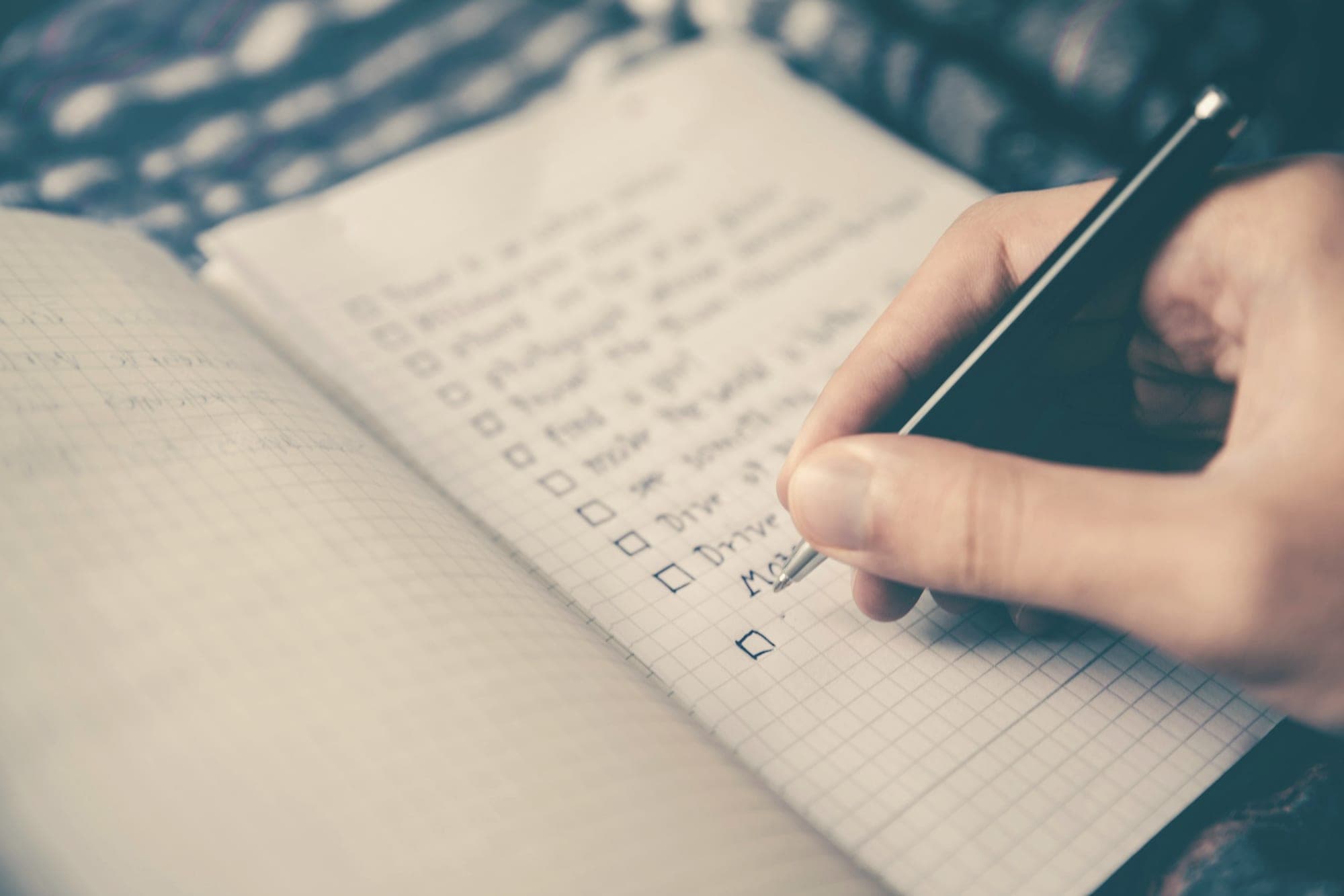A hand writing a checklist with tick boxes in a grid notebook