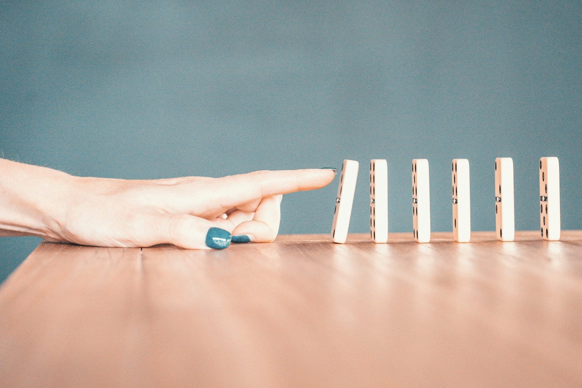 A finger about to tip the first in a row of standing dominoes