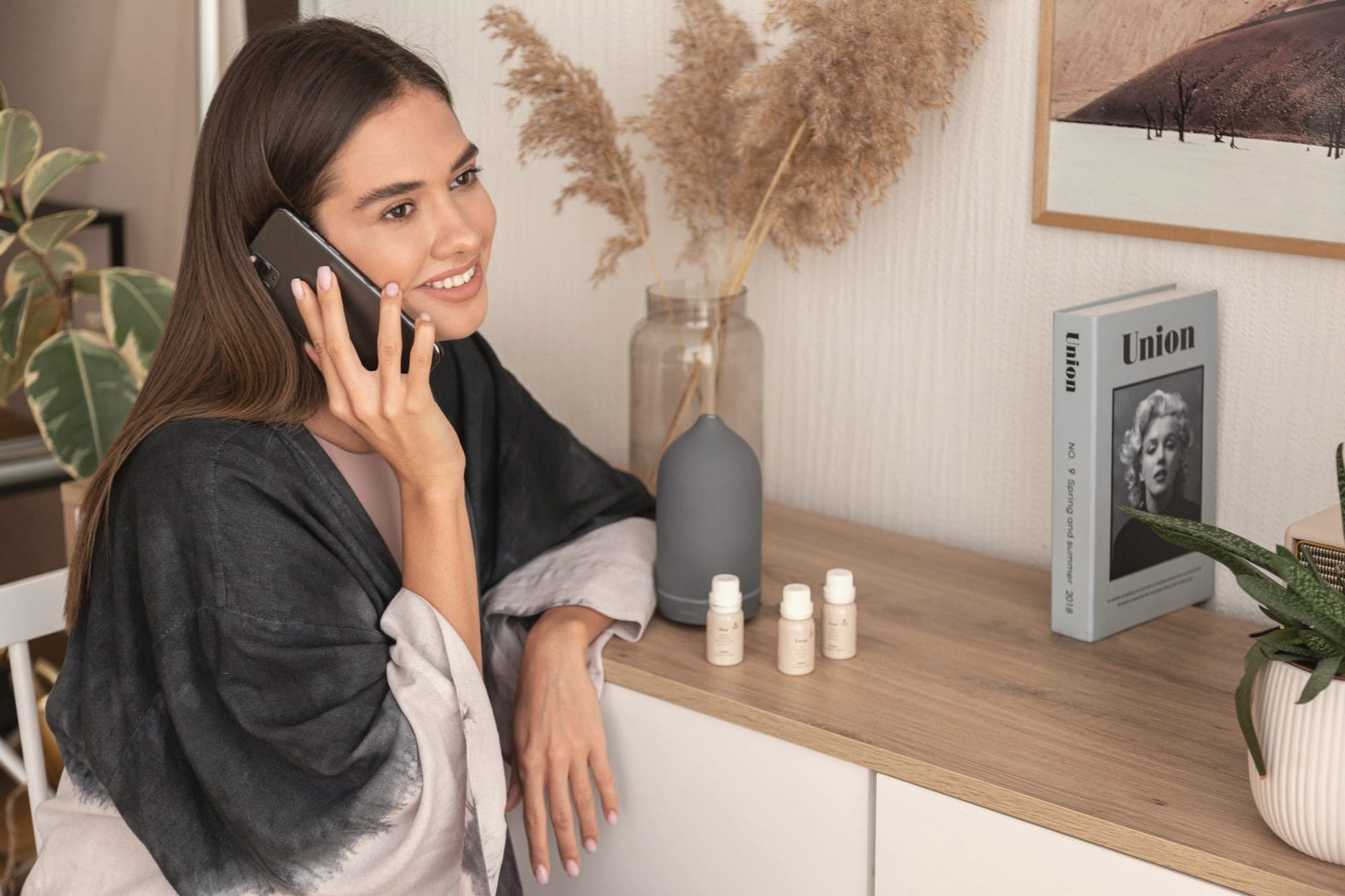 A smiling woman on a phone call, leaning on a light wooden counter