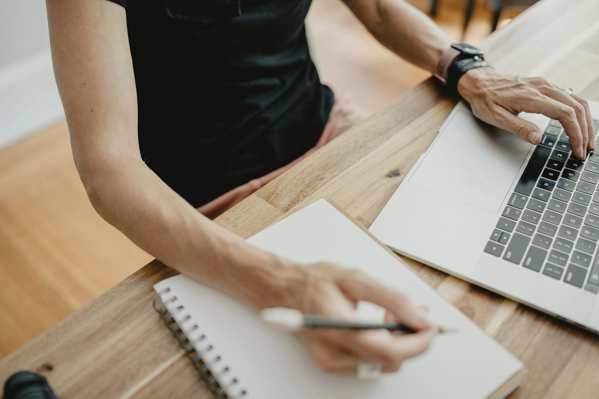 Hands taking notes in a notebook beside a laptop