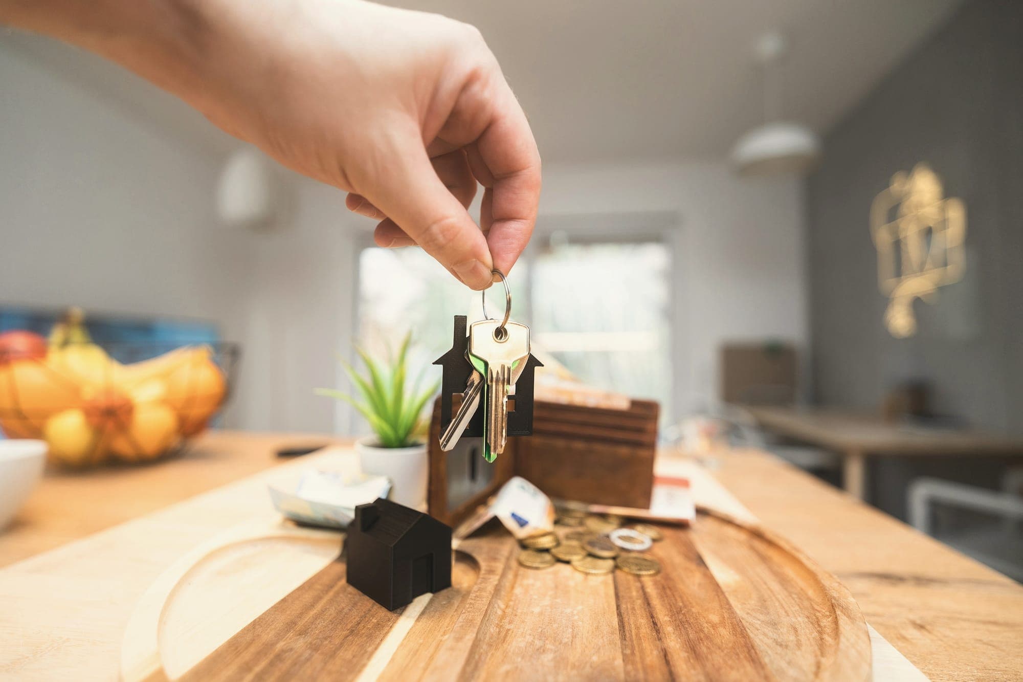 A hand holding up house keys over a kitchen table